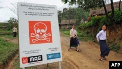 ນັກ​ຮຽນ​ຍ່າງ​ຜ່ານ​ປ້າຍ​ເຕືອນ​ເຂດ​ທີ່​ກຳ​ລັງ​ຢູ່​ພາຍ​ໃຕ້​ການ​ເກັບ​ກູ້​ລະ​ເບີດ ໂດຍ​ກຸ່ມ​ເກັບ​ກູ້​ລະ​ເບີດ UXO. ແຂວງ​ຊຽງ​ຂວາງ. 3 ເມ​ສາ 2008.