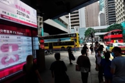 FILE - People walk past a bank's electronic board showing the Hong Kong share index at Hong Kong Stock Exchange, Oct. 5, 2020.