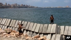 In this August 8, 2019, photo, workers prepare to place cement blocks to reinforce the sea wall against rising water levels on the corniche in Alexandria, Egypt. (AP Photo/Maya Alleruzzo)