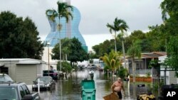 Residents clear debris from a flooded street in the Driftwood Acres Mobile Home Park in the shadow of the Guitar Hotel at Seminole Hard Rock, in the aftermath of Tropical Storm Eta, Nov. 10, 2020, in Davie, Fla.