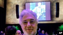 Tenor Placido Domingo poses for a photo against the backdrop of himself as a younger singer as Verdi's "Otello," Sunday, Apr 28, 2019, at the Metropolitan Opera, in New York. Domingo has starred on the stage of the Metropolitan Opera for a whopping 50 years, and is still singing.