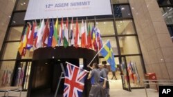 Para pekerja memasang bendera Swedia dan bendera Inggris di ruang pers dalam KTT Uni Eropa-ASEM di Brussels, Belgia, 19 Oktober 2018.