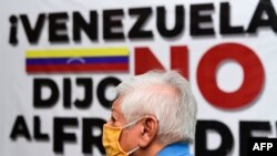 Un hombre con mascarillas pasa frente a un cartel que dice "Venezuela dijo no al fraude" mientras escucha al líder opositor venezolano Juan Guaidó durante el lanzamiento de una consulta popular. Caracas, Venezuela. Diciembre 8, 2020.