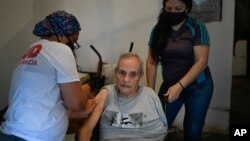 Un trabajador de la salud inocula a un anciano con una dosis de la vacuna Sputnik V COVID-19, en su casa del barrio 23 de Enero en Caracas. Junio 12, 2021.