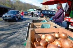 Workers from Sarver farms, right, wear protective masks, beside the onions, potatoes and vegetables they are selling to patrons driving by in their cars at the Greensburg Farmers Market opening day, April 25, 2020, in Greensburg, Pa.