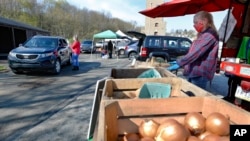 Workers from Sarver farms, wear protective masks, beside the onions, potatoes and vegetables they are selling to patrons driving by in their cars at the Greensburg Farmers' Market opening day, April 25, 2020, in Greensburg, Pa.
