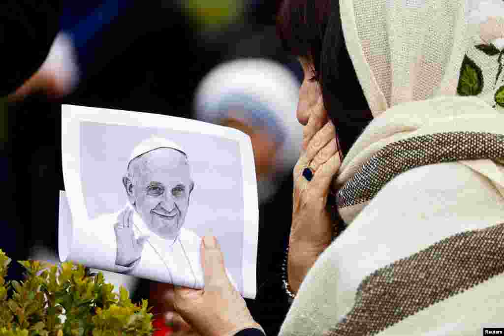 A person holds a picture of Pope Francis near the statue of late Pope John Paul II outside Gemelli Hospital where Pope Francis is admitted to continue treatment, in Rome, Italy.