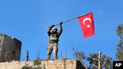 FILE -- In this Sunday, Jan. 28, 2018 file photo, a soldier waves a Turkish flag as Turkish troops secure Bursayah hill, near the Kurdish-held enclave of Afrin.