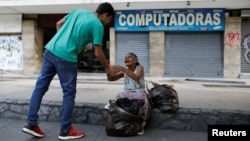 Mariano Marquez (L), a volunteer of Make The Difference (Haz La Diferencia) charity initiative, gives a cup of soup and an arepa to a homeless woman in a street of Caracas, March12, 2017. 