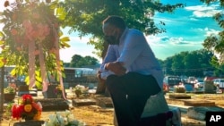 FILE - Will Boyd kneels at the grave of a family member who died after contracting the coronavirus, June 20, 2020, in Montgomery, Ala. He has lost multiple family members to COVID-19.