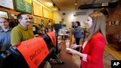 FILE - Molly Kepner, right, smiles after hearing the news of her discount from Tom Grover at The Works Bakery Café in Concord, N.H., April 12, 2016. The New Hampshire bakery chain gave women a break in honor of Equal Pay Day, charging them 79 percent of their bill. 