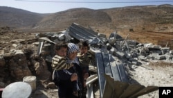 FILE - A Palestinian woman carries her children after the destruction of her home in Aqraba village, near the settlement of Itamar, Nablus, West Bank.