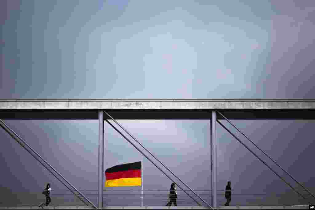 عبور مردم از پل عابر پیاده مقابل ساختمان پارلمان آلمان در یک روز ابری در برلین