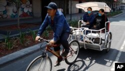 Dua penumpang becak mengenakan masker wajah di Mexico City, 6 April 2020.