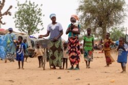 FILE - Women and children walk in a makeshift site for displaced people in Kongoussi, Burkina Faso, June 4, 2020.
