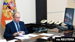 Vladimir Putin ari mu biro bye i Moscou mu Burusiya. Aha ari mu kiganiro kuri conference video n'abakozi bo mu by'ubuzima.