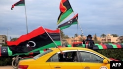 FILE - Libyans wave national flags from a cab in the capital, Tripoli, Feb. 25, 2021, during celebrations commemorating the 10th anniversary of the 2011 revolution that toppled longtime dictator Moammar Gadhafi.