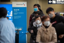 FILE - Travelers wearing face masks line up to check in for an American Airlines flight to Los Angeles at Beijing Capital International Airport in Beijing, Jan. 30, 2020.