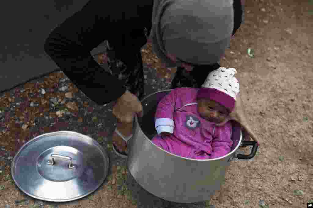 A Syrian mother carries her baby girl in a cooking pot at Ritsona refugee camp north of Athens, Greece.