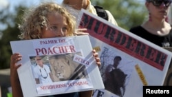 Protesters hold signs during a rally outside the River Bluff Dental clinic against the killing of a famous lion in Zimbabwe, in Bloomington, Minnesota, July 29, 2015. 