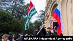 In this photo taken from video released by the AIASHARA Independent Agency, protesters gather around Abkhazian and Russian flags outside the parliament building of the Georgian separatist region of Abkhazia, Nov. 15, 2024.