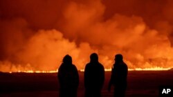 La gente observa cómo el cielo nocturno se ilumina debido a la erupción de un volcán en Grindavik, en la península de Reykjanes, Islandia, el lunes 18 de diciembre de 2023.