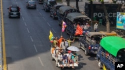 A vehicle with Myanmar and military flags and supporters of the Myanmar military and the military-backed Union Solidarity and Development Party passes by a row of police trucks with police security onboard parked near the Kyauktada police station in…
