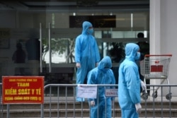 FILE - Medical workers in protective suits stand outside a quarantined building amid the COVID-19 outbreak in Hanoi, Vietnam, January 29, 2021.