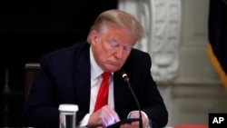 FILE - President Donald Trump looks at his phone during a roundtable in the State Dining Room of the White House, June 18, 2020, in Washington. 