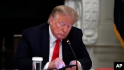 FILE - President Donald Trump checks his phone during a roundtable discussion in the State Dining Room of the White House, in Washington, June 18, 2020.