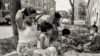 Cambodian women and children relax and play between the street and sidewalk outside their apartment building in the 1990s along West Argyle Street in the Uptown neighborhood of Chicago. (Stuart Isett)