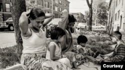 Cambodian women and children relax and play between the street and sidewalk outside their apartment building in the 1990s along West Argyle Street in the Uptown neighborhood of Chicago. (Stuart Isett)