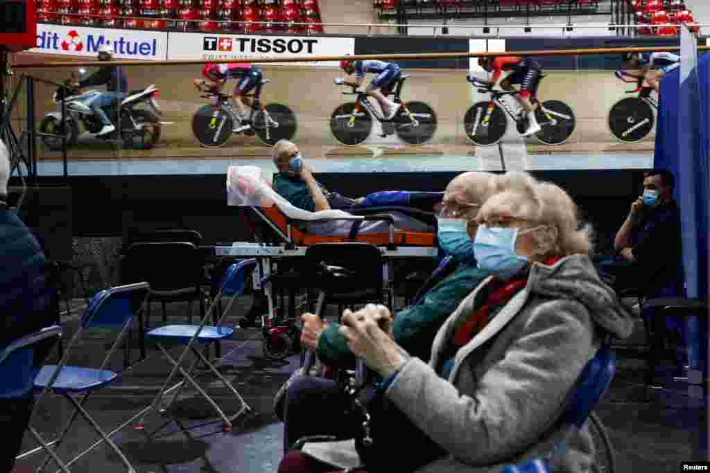 France&#39;s national cycling team trains as people wait to get a dose of the Pfizer-BioNTech COVID-19 vaccine at the indoor Velodrome National of Saint-Quentin-en-Yvelines in Montigny-le-Bretonneux, southwest of Paris, France.