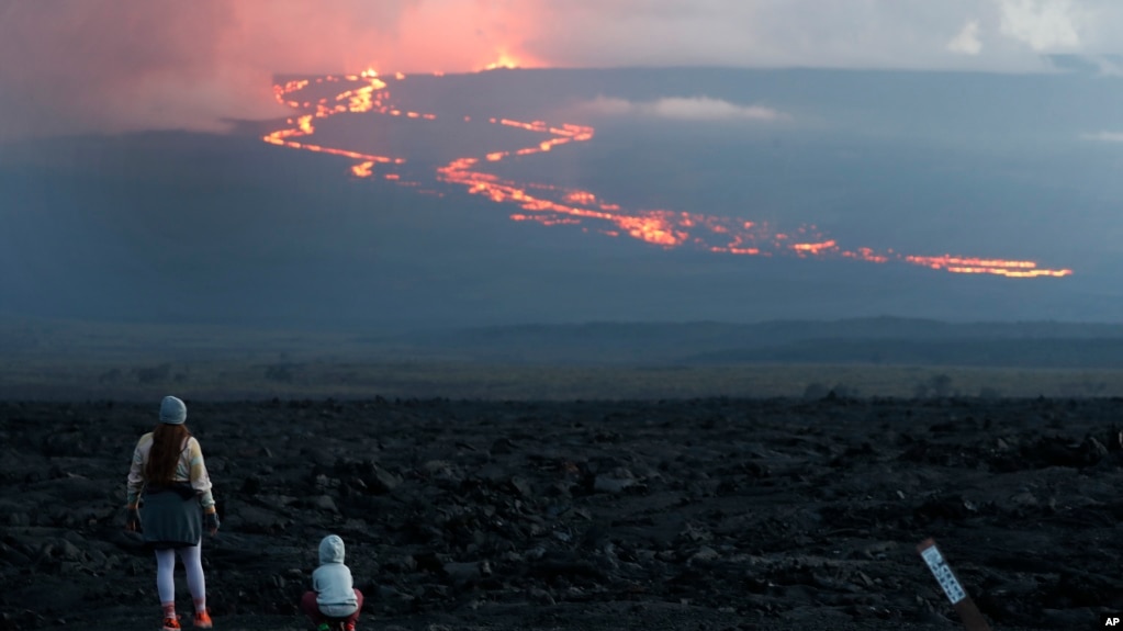 In this file photo, onlookers watch the lava flow down the mountain from the Mauna Loa eruption, Tuesday, Nov. 29, 2022, near Hilo, Hawaii. (AP Photo/Marco Garcia, File)