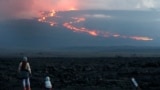 In this file photo, onlookers watch the lava flow down the mountain from the Mauna Loa eruption, Tuesday, Nov. 29, 2022, near Hilo, Hawaii. (AP Photo/Marco Garcia, File)