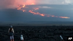 In this file photo, onlookers watch the lava flow down the mountain from the Mauna Loa eruption, Tuesday, Nov. 29, 2022, near Hilo, Hawaii. (AP Photo/Marco Garcia, File)