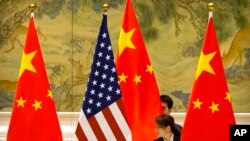 Seorang pegawa sedang memperbaiki posisi bendera AS dan China sebelum sesi pembukaan pembicaraan dagang antara perwakilan AS dan China di Beijing, 14 Februari 2019. (Foto: Mark Schiefelbein/AP Photo)