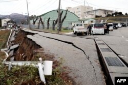 People stand next to large cracks in the pavement after evacuating into a street in the city of Wajima, Ishikawa prefecture of Japan on Jan. 1, 2024, after a major 7.5 magnitude earthquake struck the Noto region.