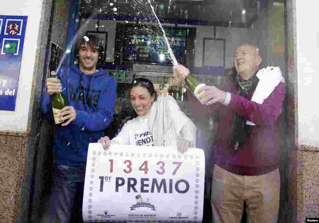 Lottery seller Raquel Carrasco (C) holds a sign with the winning number of Spain&#39;s Christmas Lottery &quot;El Gordo&quot; as employees spray champagne in La Eliana near Valencia. The total prize money of 2.4 billion euros is split into thousands of cash prizes among hundreds of winning numbers.