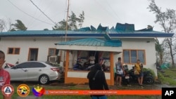 In this photo provided by Philippine Coast Guard, its members stand outside their building damaged by Typhoon Yinxing in Santa Ana, Cagayan province, northern Philippines, Nov. 7, 2024.