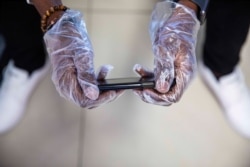 A passenger wears gloves to use his phone while waiting to board a flight at Toussaint Louverture International Airport, March 14, 2020, in Port-au-Prince, Haiti. As of Saturday, there were no reported cases of COVID-19 in Haiti.