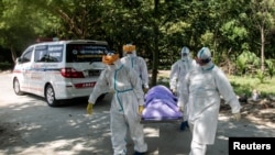 ရန်ကုန်မြို့တွင် ကိုဗစ်ကြောင့်သေဆုံးသူတစ်ဦးကို သဂြိုၤဟ်ဖို့ သယ်ဆောင်နေကြတဲ့ PPE ဝတ်စုံဝတ် ပရဟိတလုပ်သားများ။ (နိုဝင်ဘာ ၂၅၊ ၂၀၂၀)