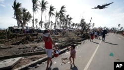 ARCHIVO- En esta fotografía de archivo del 11 de noviembre de 2013, los sobrevivientes observan cómo un avión militar C-130 llega a la ciudad de Tacloban, devastada por un tifón, en la provincia de Leyte, en el centro de Filipinas.