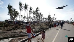 FILE- In this Nov. 11, 2013, file photo, survivors look as a military C-130 plane arrives at typhoon-ravaged Tacloban city, Leyte province central Philippines. 