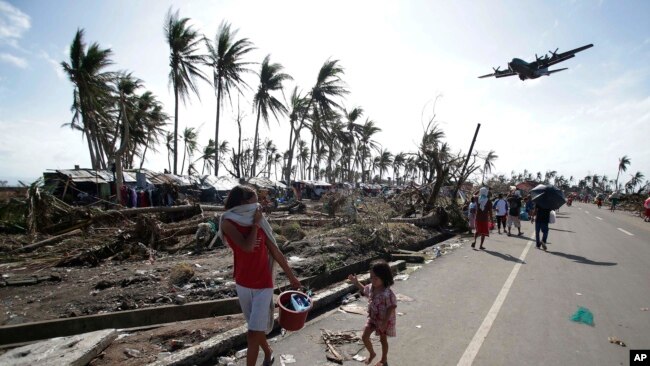 FILE- In this Nov. 11, 2013, file photo, survivors look as a military C-130 plane arrives at typhoon-ravaged Tacloban city, Leyte province central Philippines.