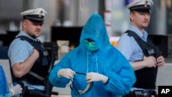 A Chinese tourist prepares for his flight to China as two German police officers walk by at the airport in Frankfurt, Germany, Sunday, March 29, 2020. 