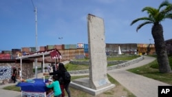 Una familia empuja un carrito de bocadillos más allá de una losa del Muro de Berlín, exhibida cerca del muro fronterizo que separa a Estados Unidos de México, en Tijuana, México, el viernes 25 de agosto de 2023.