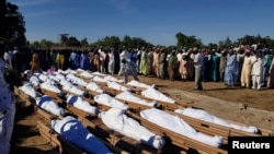 FILE - Men gather near bodies of people who were killed in a militant attack, during a mass burial at Zabarmari, in the Jere local government area of Borno state, in northeast Nigeria, Nov. 29, 2020.