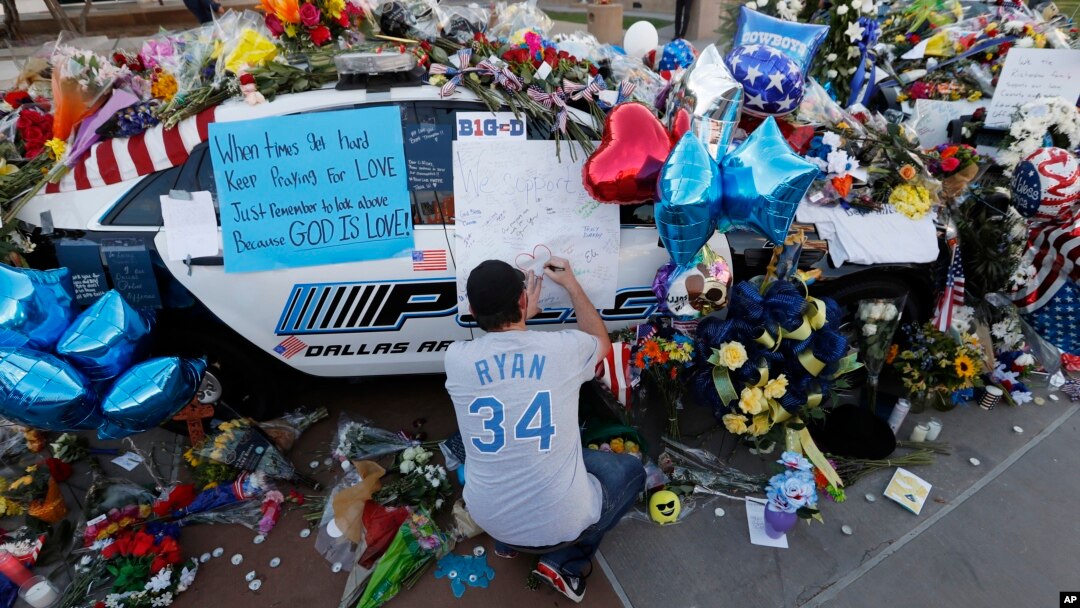 Tracy St. Romain leaves a note on a patrol car at a makeshift memorial in front of the Dallas (Texas) police department, July 9, 2016. The memorial honors five officers fatally shot by a sniper Thursday evening. 