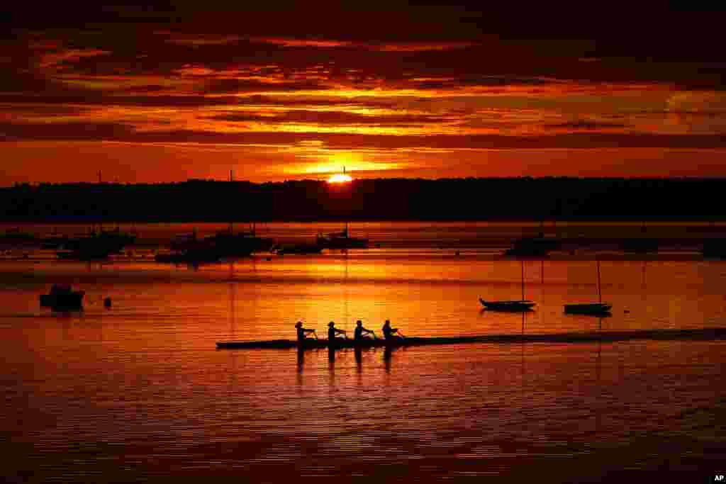 A quad scull of rowers begin their workout on Casco Bay as the sun starts to peak over Great Diamond Island in Portland, Maine.